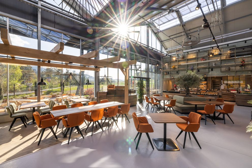 Glass restaurant dining room with skylight roof, wood beams, and orange chairs
